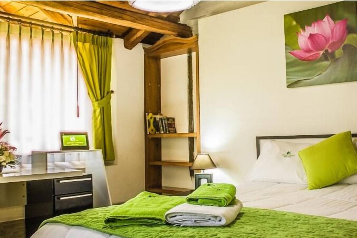 Habitación de hotel con cama, escritorio, silla, lámpara y un cuadro de una flor de loto.