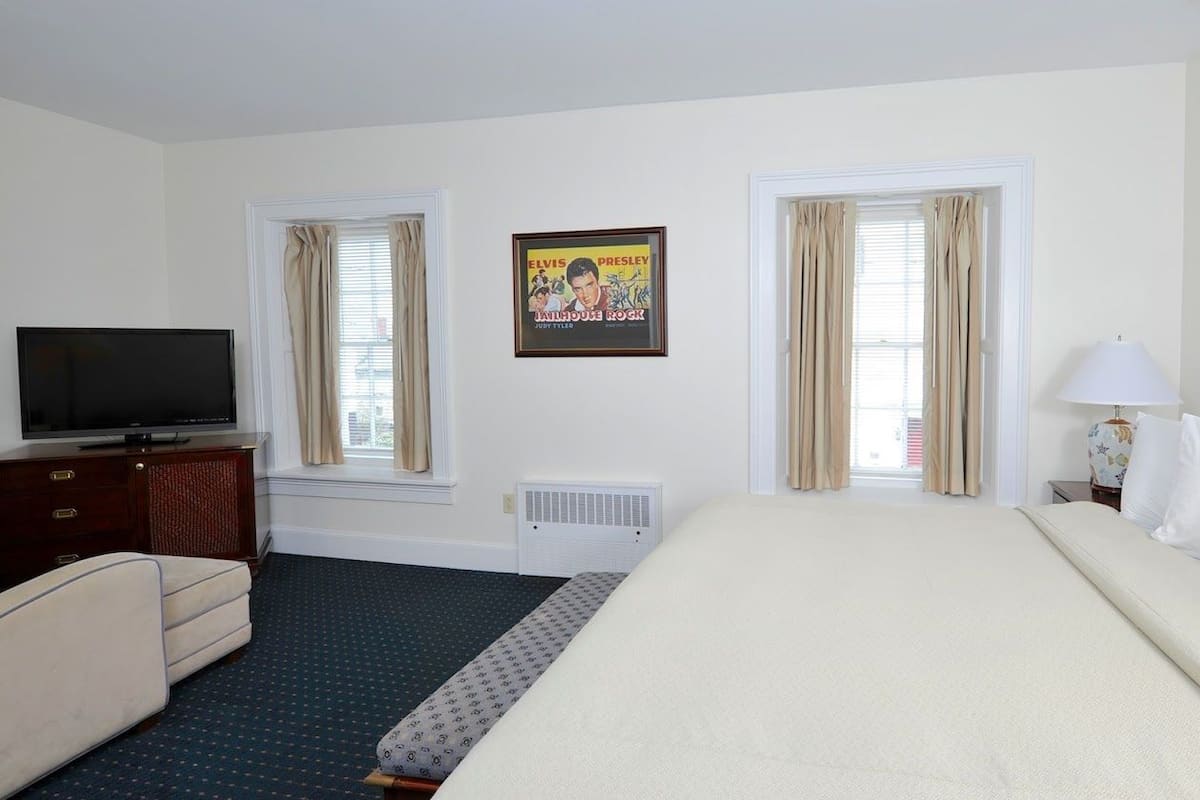 Une chambre d’hôtel avec un lit, une télévision, une commode et une fenêtre avec des rideaux.