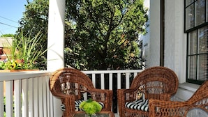 A wicker patio with two chairs and a table, white railings, and a large tree in the background. - Jailhouse Inn (Newport)