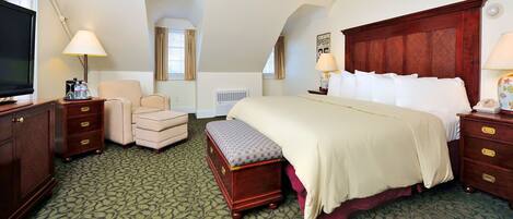 Une chambre d’hôtel avec un grand lit, un bureau avec une lampe, une chaise, une petite table avec une lampe, un téléviseur et une fenêtre avec des rideaux.