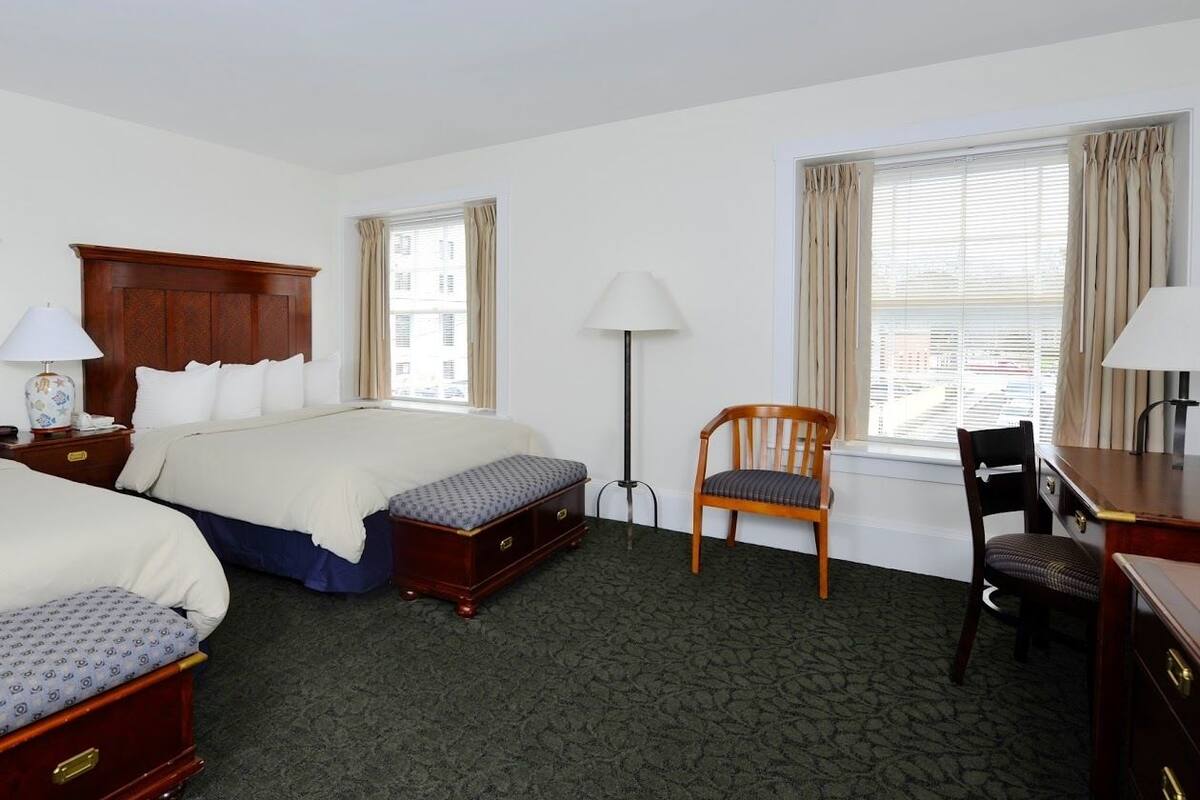 Une chambre d’hôtel avec deux lits, un bureau, une chaise et une lampe.