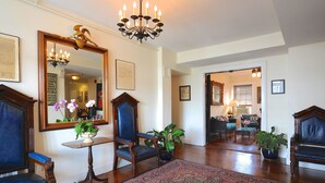 A spacious living room with a large mirror, a chandelier, and a wooden floor. There are several chairs and a table with a vase of flowers. - Jailhouse Inn (Newport)