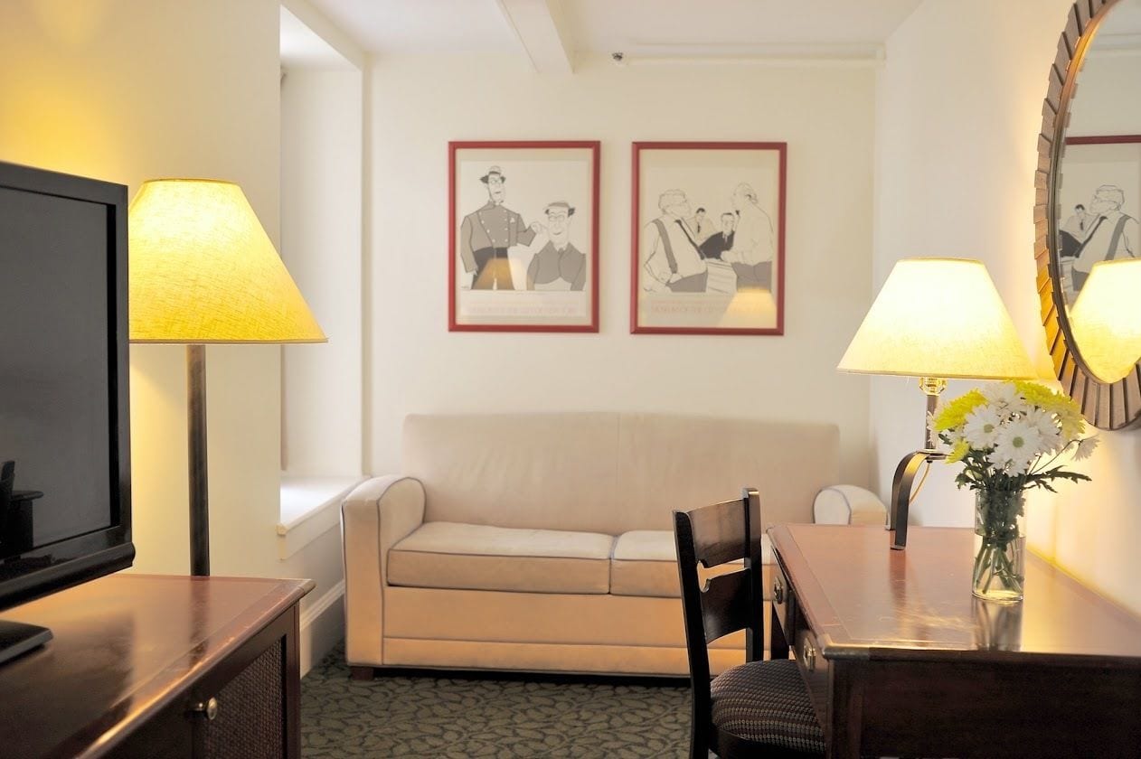 Une chambre d’hôtel comprenant un canapé, une table à manger avec une chaise, un téléviseur, deux lampes et deux tableaux encadrés accrochés au mur.