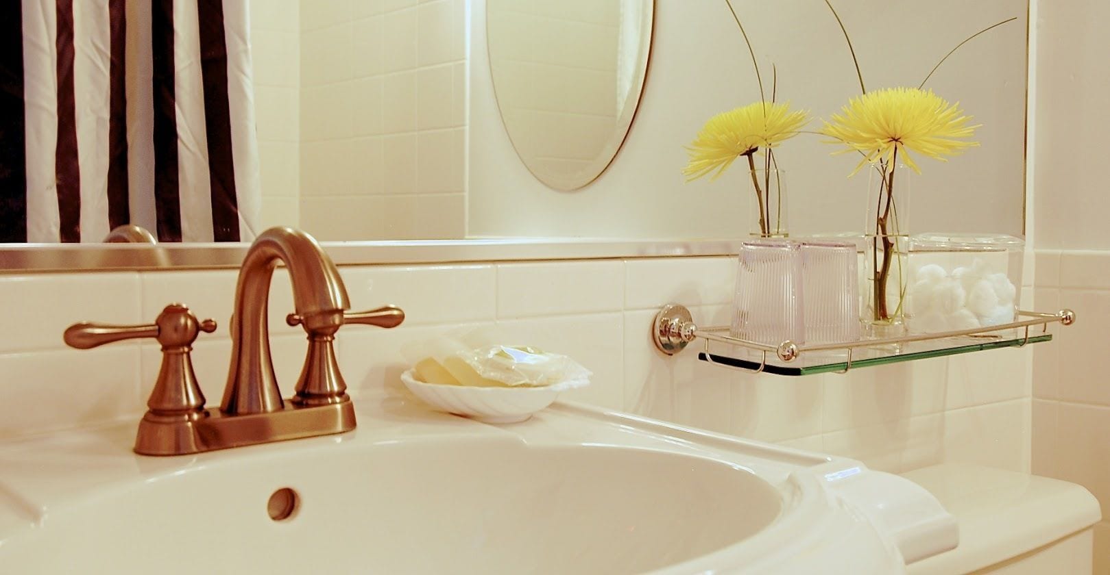 Un baño con lavamanos blanco, grifo de cobre y repisa de vidrio con artículos de aseo.