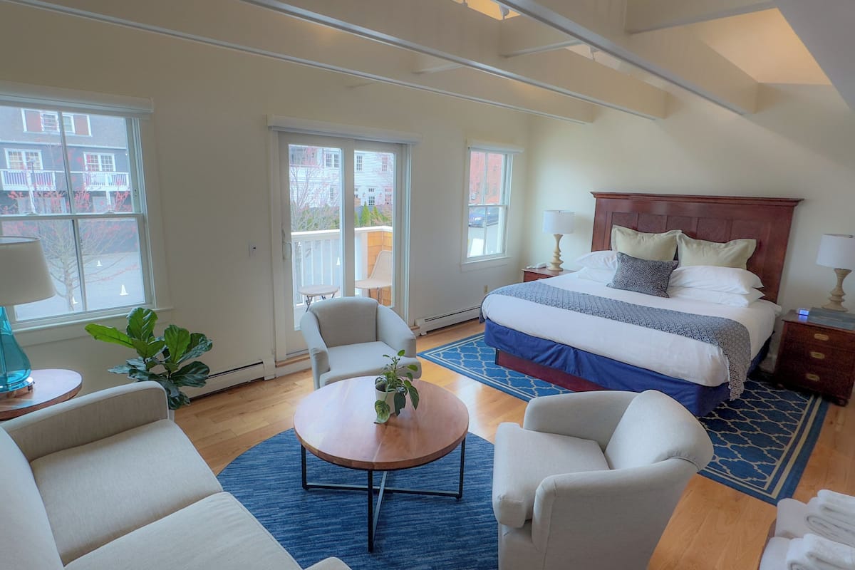 A hotel room with a large bed, a sitting area with a coffee table, a sofa, and a balcony with a view of buildings.