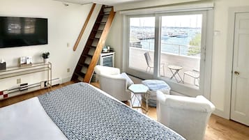 A spacious bedroom with a large bed, a TV, a ceiling fan, and a balcony with a view of the water.