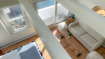 Et rum med højt til loftet, stort vindue, sofa, lille bord og et mønstret tæppe.