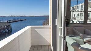 A balcony with a view of a dock and water, a white railing, and a sofa with cushions. - Harborside Inn (Newport)