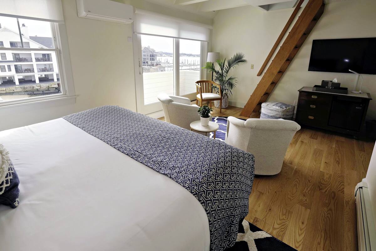 A hotel room with a bed, a chair, a small table, a TV, and a staircase.