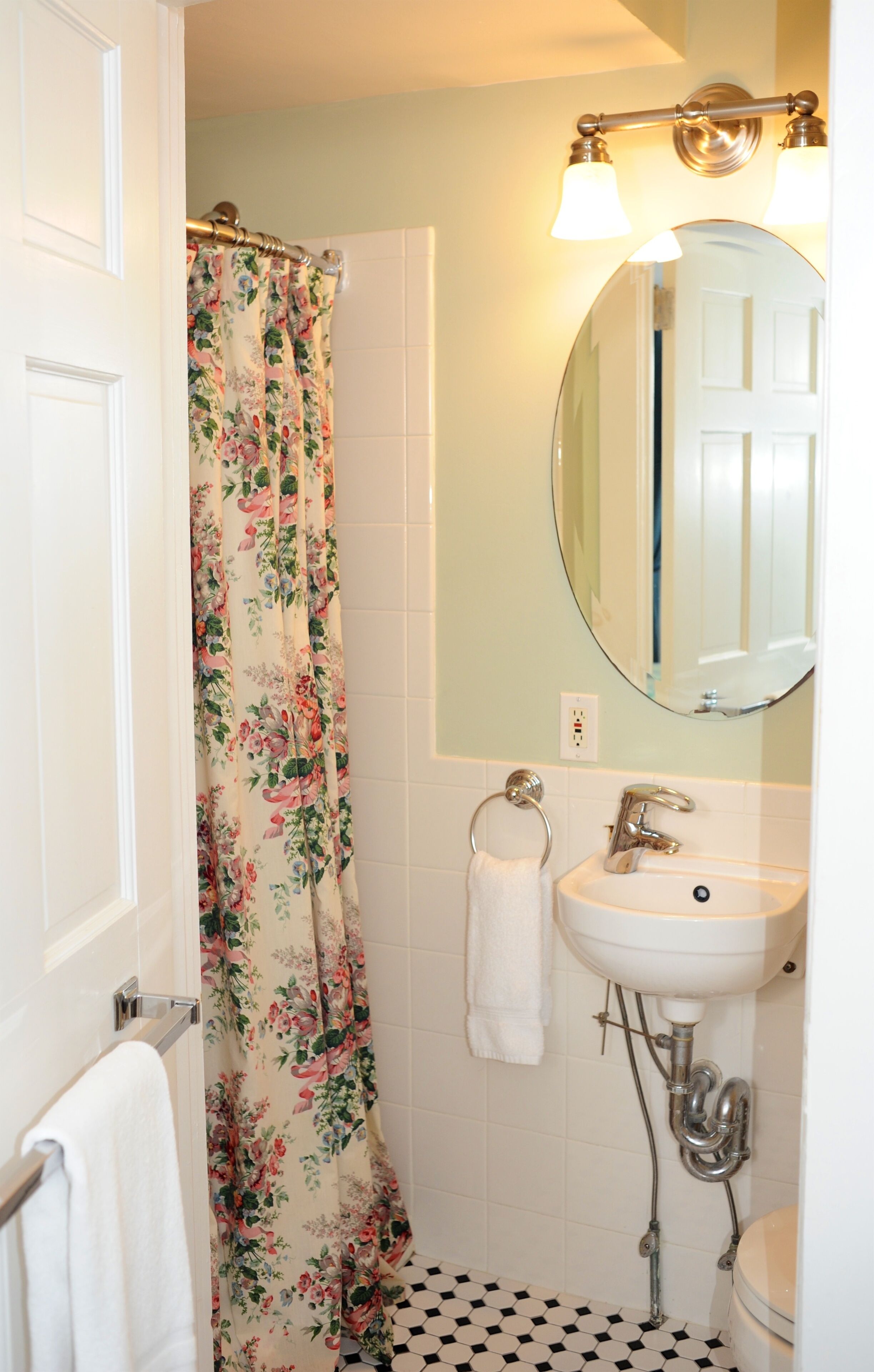 A bathroom with a shower curtain, a sink, a mirror, and a toilet.