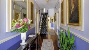 Un pasillo con una escalera, un jarrón de flores y obras de arte enmarcadas en las paredes.