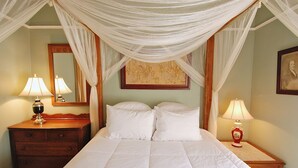 Un dormitorio con cama con dosel, dos mesitas de noche con lámparas, un aparador de madera y un espejo.