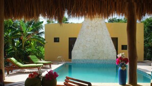 Un área de piscina con sillones reclinables, una mesa con un jarrón de flores y un muro de piedra.