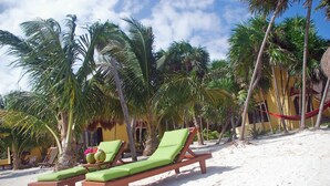 Una playa con dos sillones de madera con cojines verdes, una hamaca roja y palmeras.