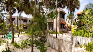 Un resort con varias edificaciones, palmeras y una zona de arena con valla de madera.