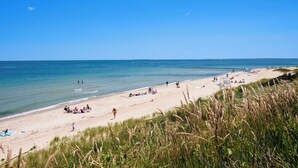 A beach with people relaxing and sunbathing, a lifeguard tower, and grassy dunes. - Pequot Hotel (Oak Bluffs)