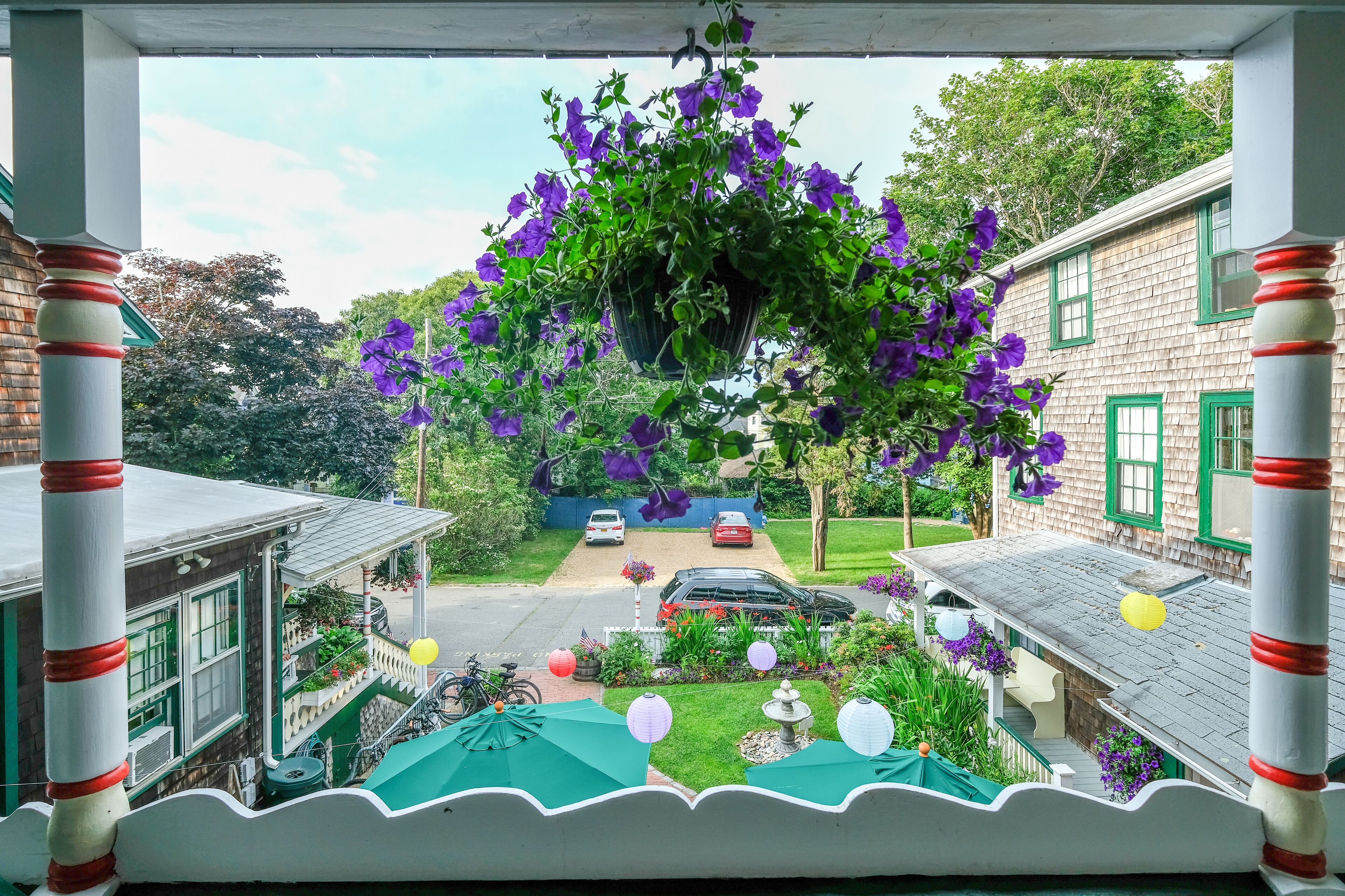 A porch with a hanging flower basket, a small garden with a fountain, and a view of a street with cars and houses.