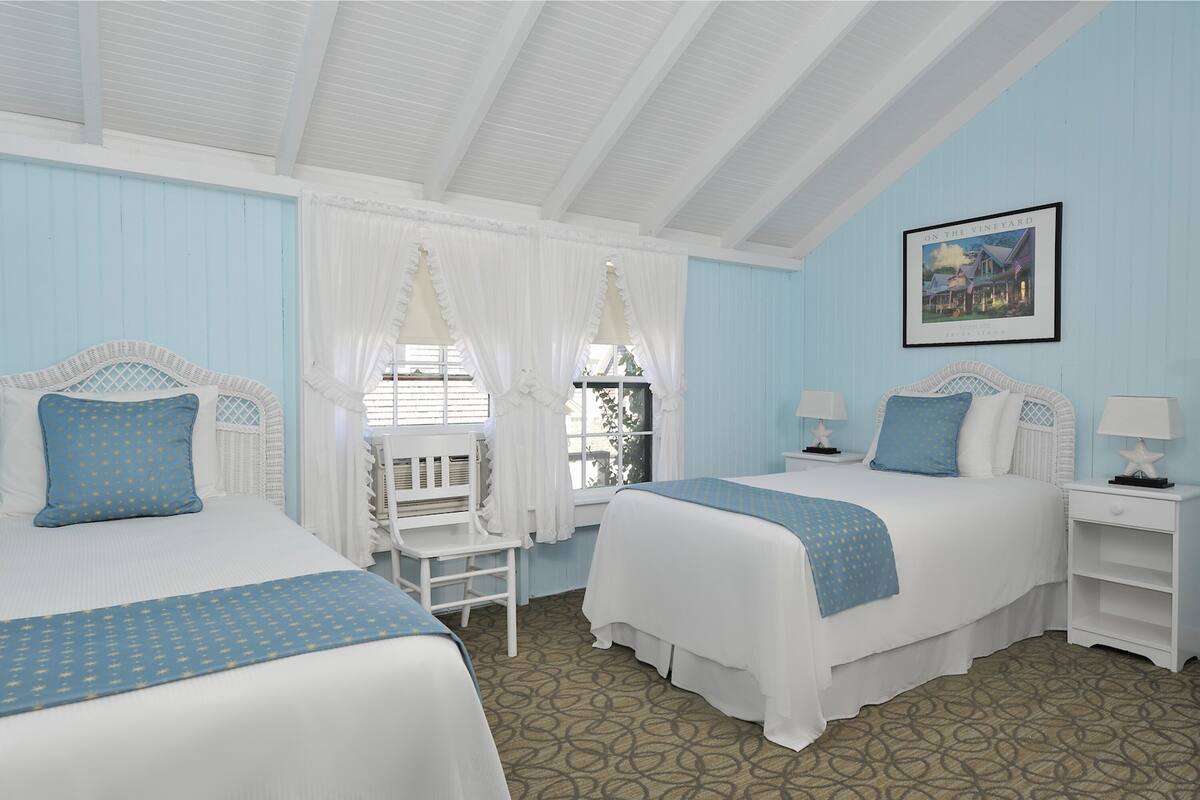 A room with two beds, white bedding, and a framed picture on the wall.