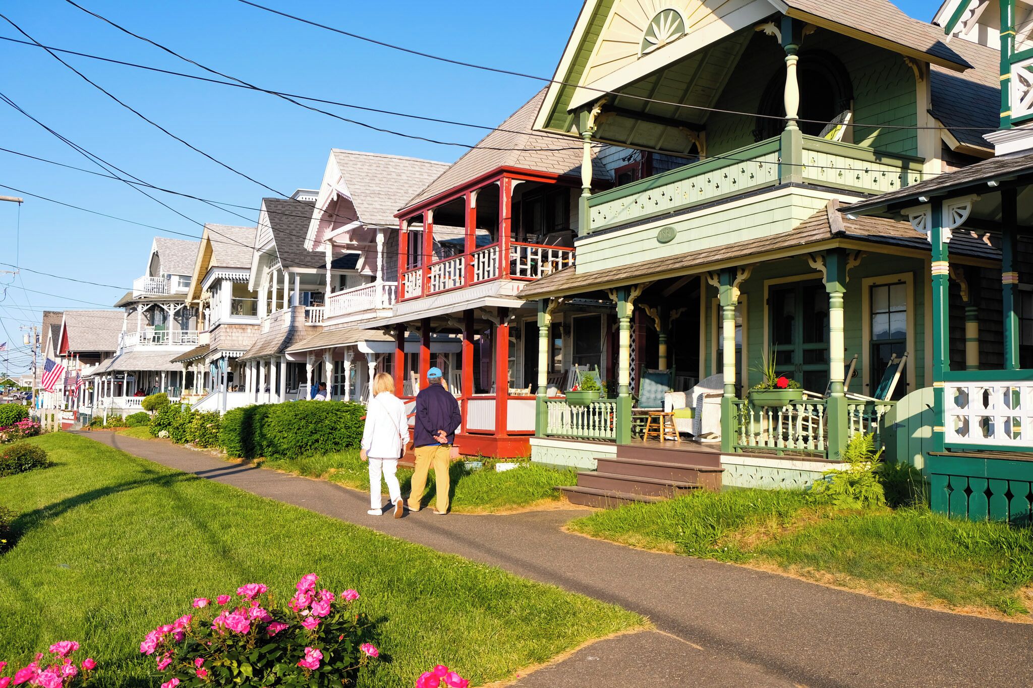 Une rangée de maisons traditionnelles en bois aux façades vertes et blanches, une allée pavée et, au premier plan, des fleurs roses.