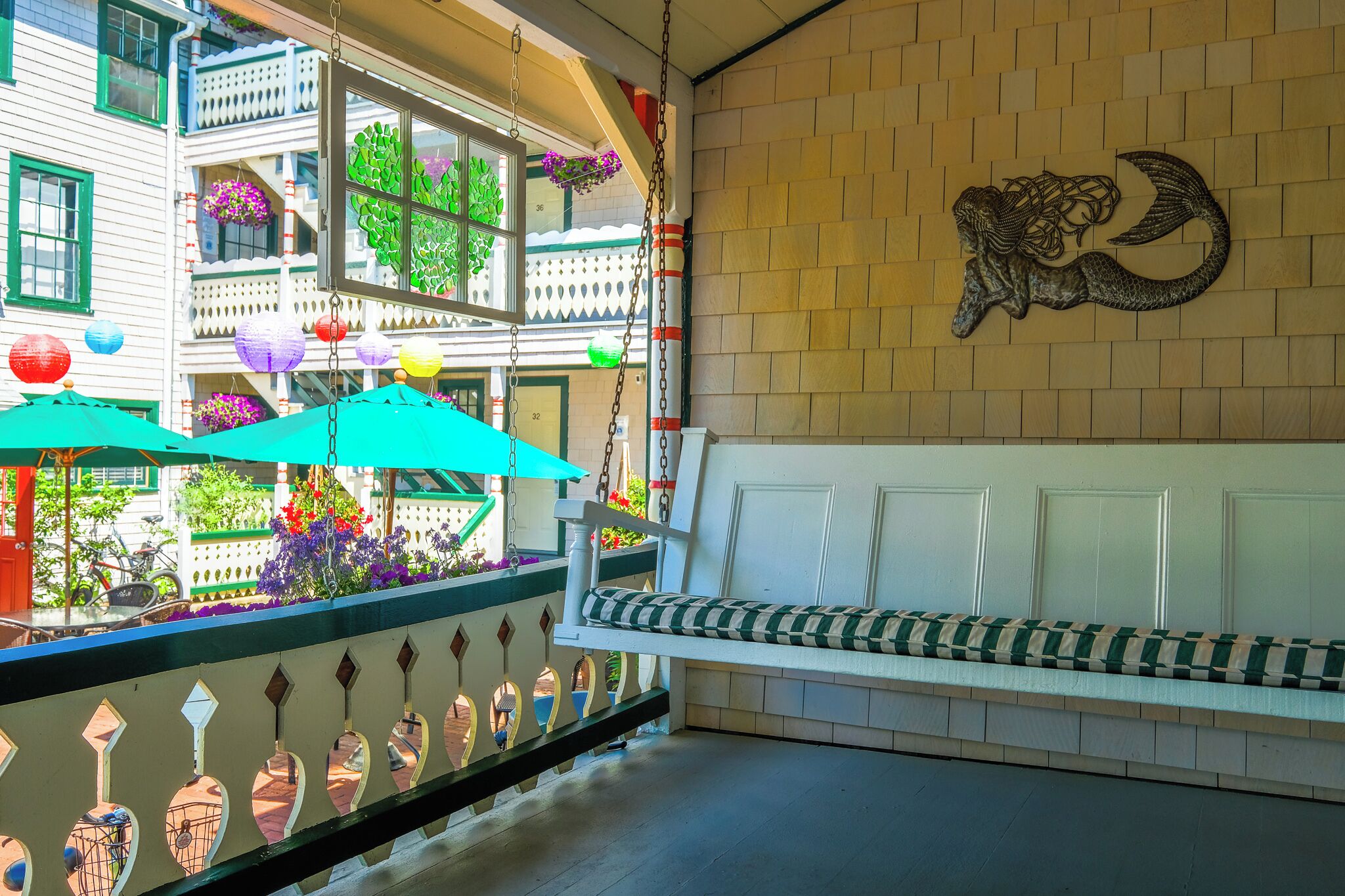 A balcony with a white bench, a decorative wall with a ram head sculpture, and hanging flower baskets.