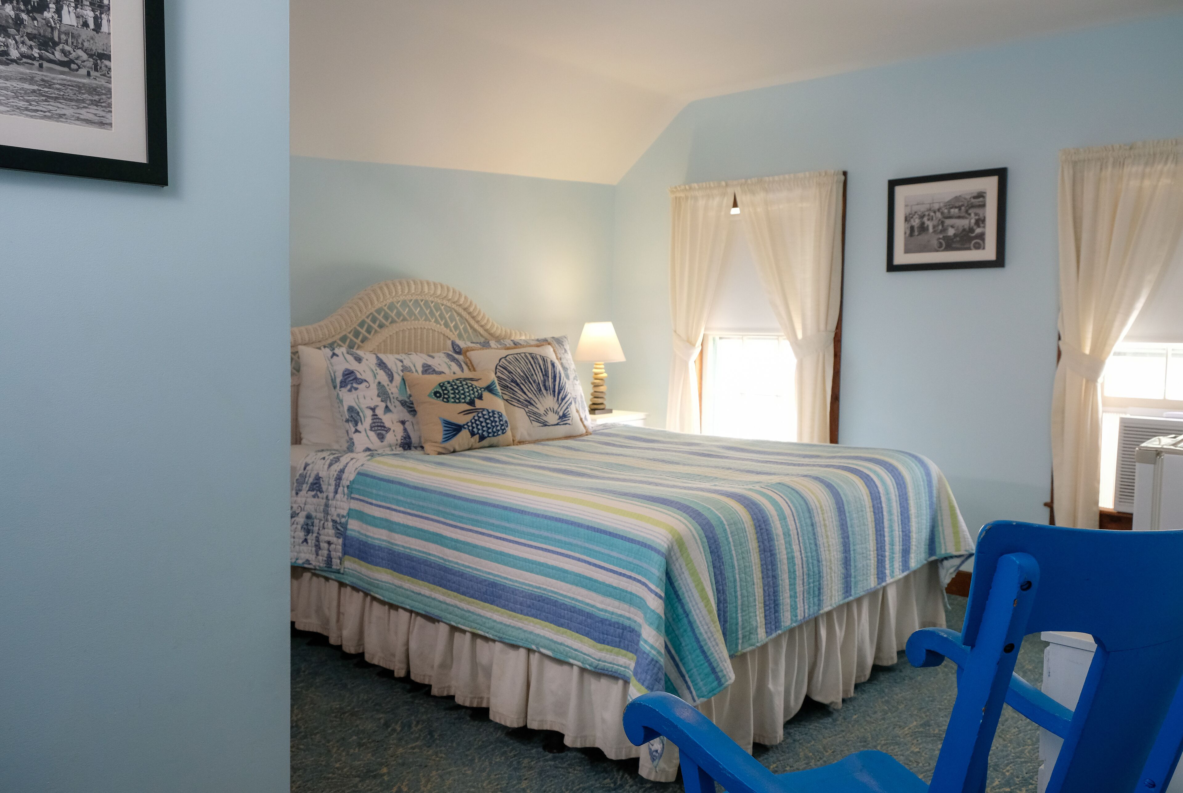 A bedroom with a bed, a nightstand, a lamp, and a blue chair.