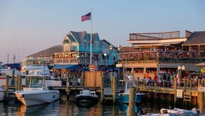 A waterfront dock with boats, a building with a balcony, and an American flag. - Pequot Hotel (Oak Bluffs)