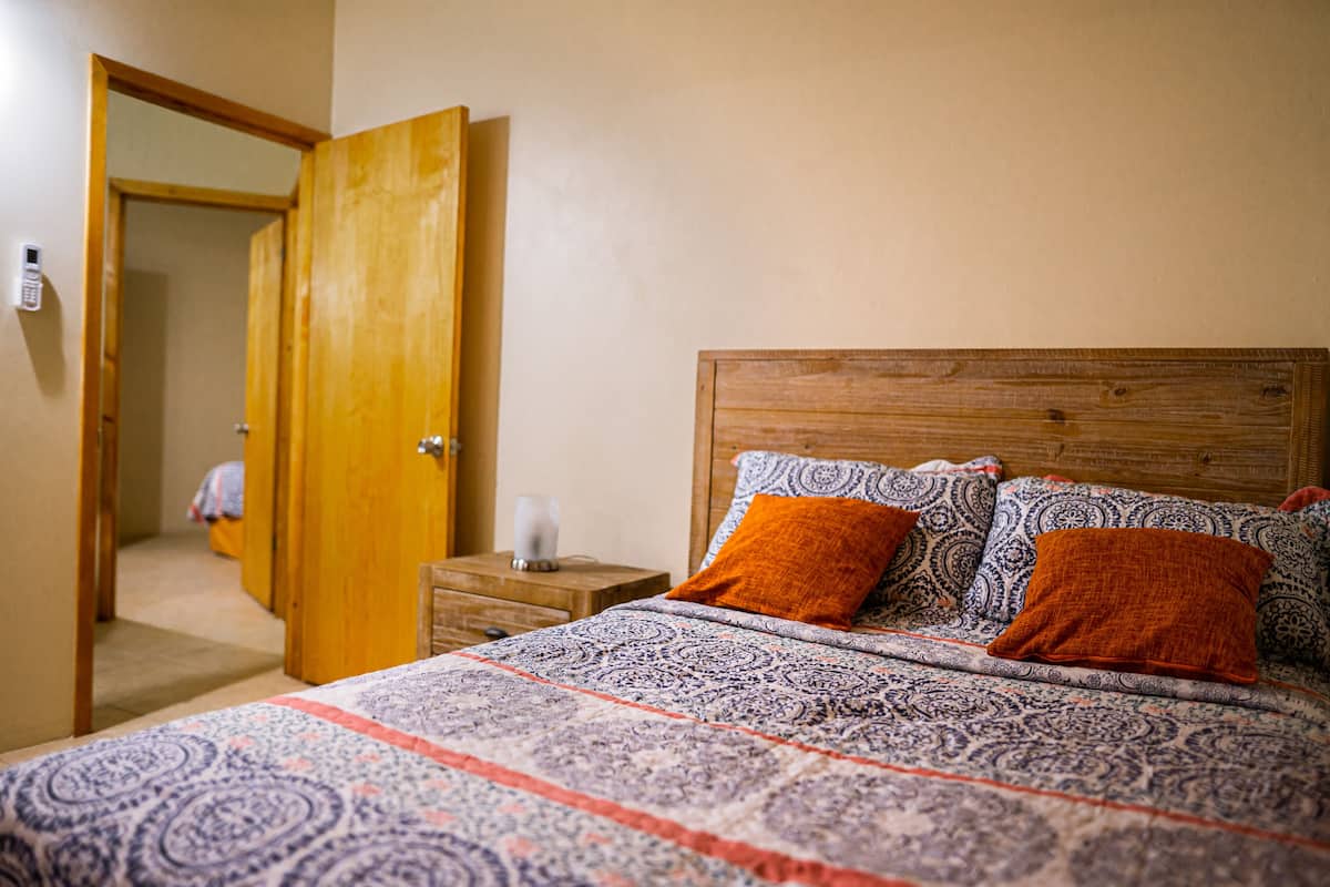 A bedroom with a wooden headboard, patterned bedding, and an open door leading to another room.