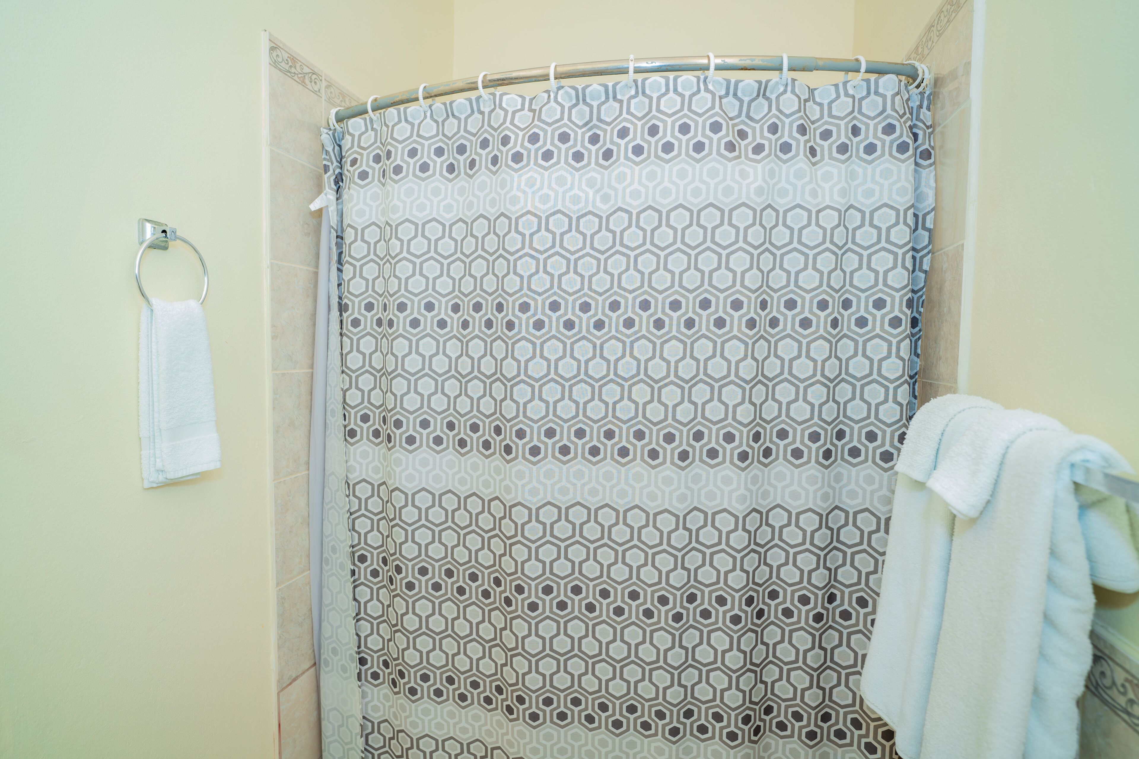 Un área de ducha con cortina de baño estampada, un aro metálico para toallas y una toalla blanca colgada en la pared.