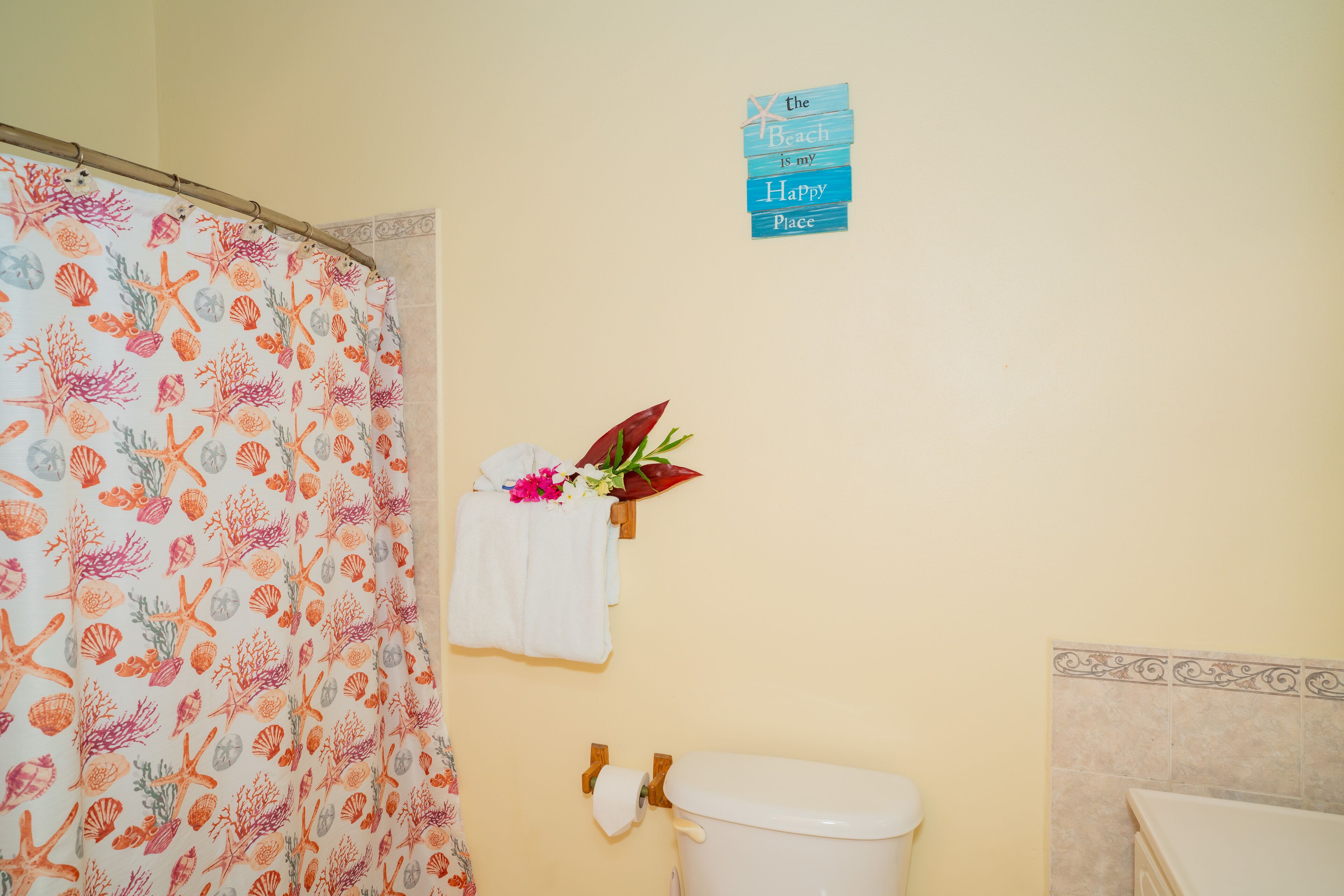 Un baño con cortina de ducha con estampado de vida marina, un inodoro, un perchero con una flor y un letrero en la pared.