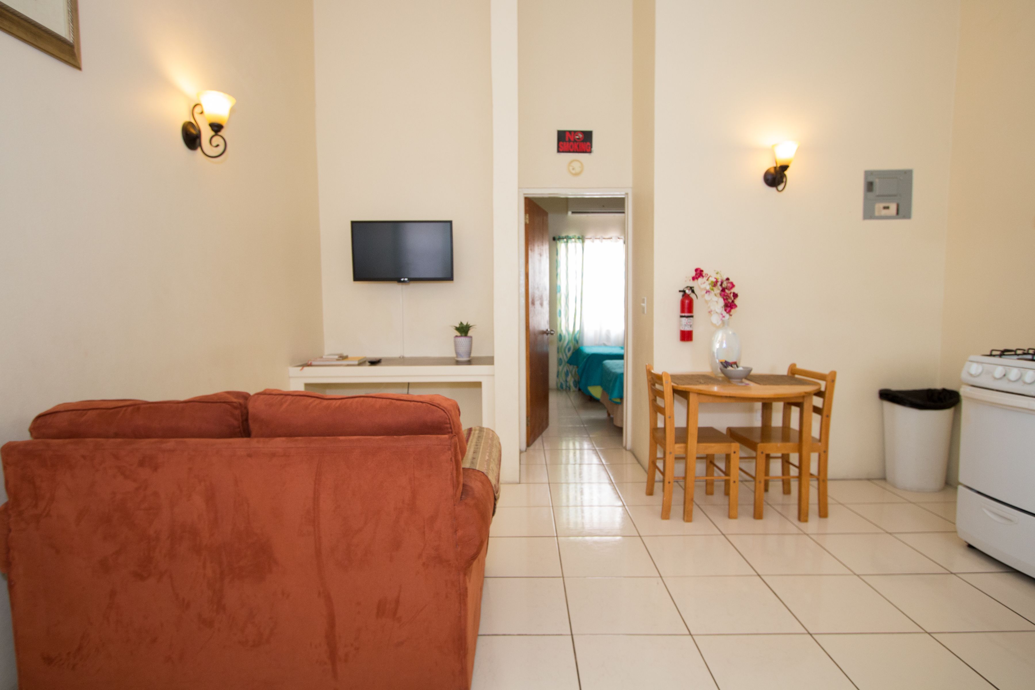 A living room with a sofa, a TV, a dining area with a table and chairs, and a kitchen with a stove.