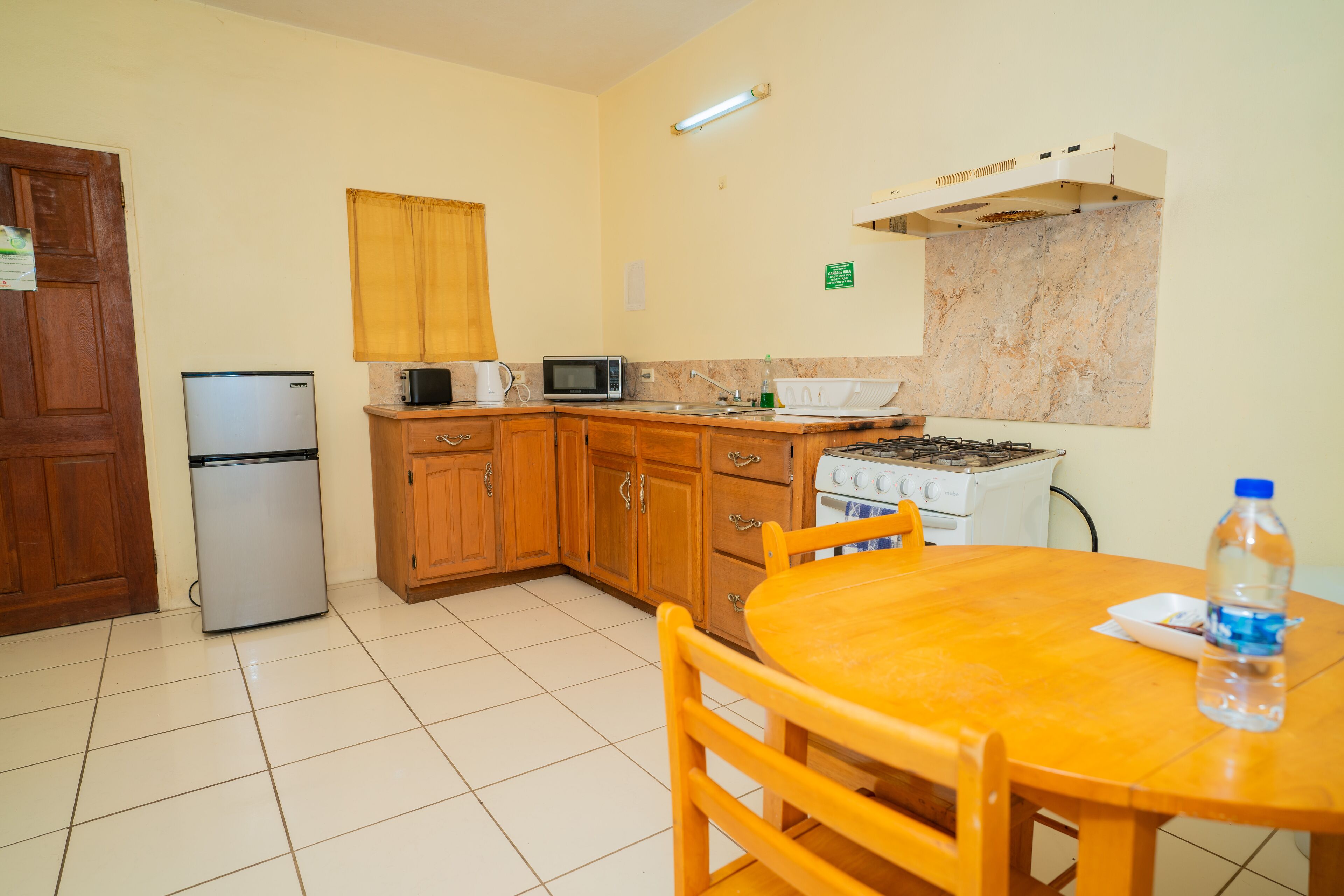 Una cocina compacta con armarios de madera, microondas, refrigerador, estufa y una mesa de comedor con sillas.