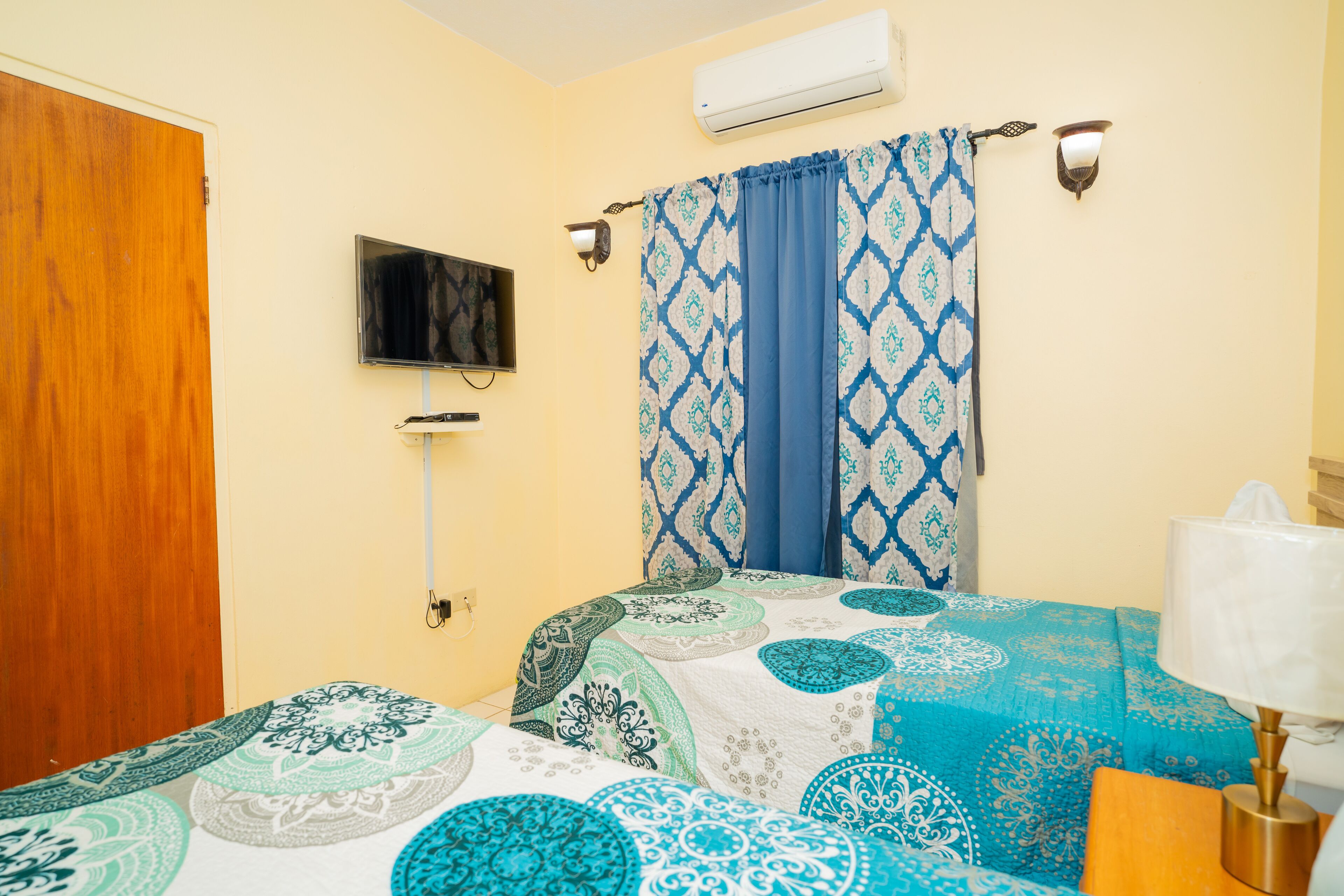 A bedroom with a bed, a TV, an air conditioner, and a lamp.