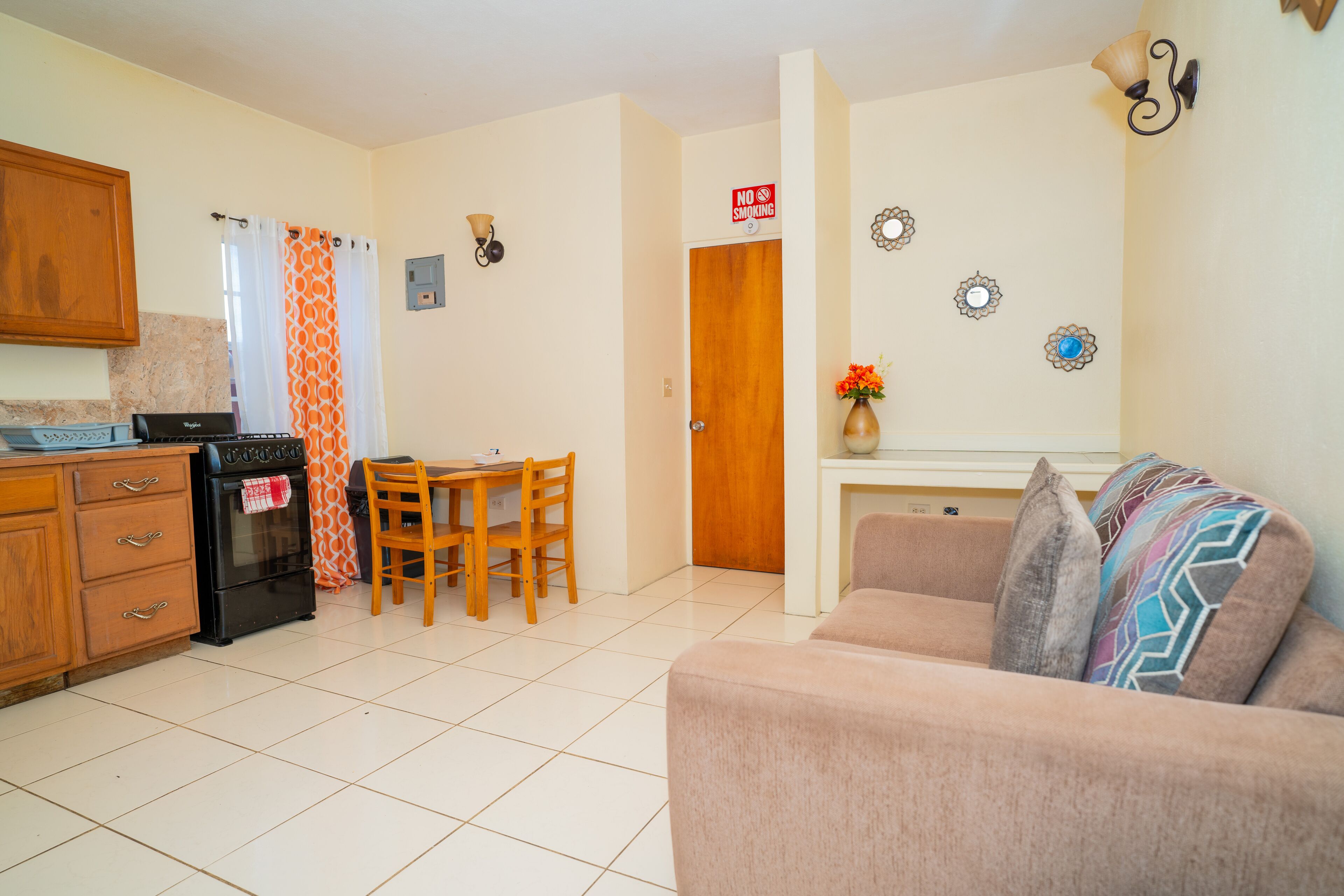 A kitchen with a stove, oven, and wooden cabinets. There is a dining table with chairs and a sofa in the living area.