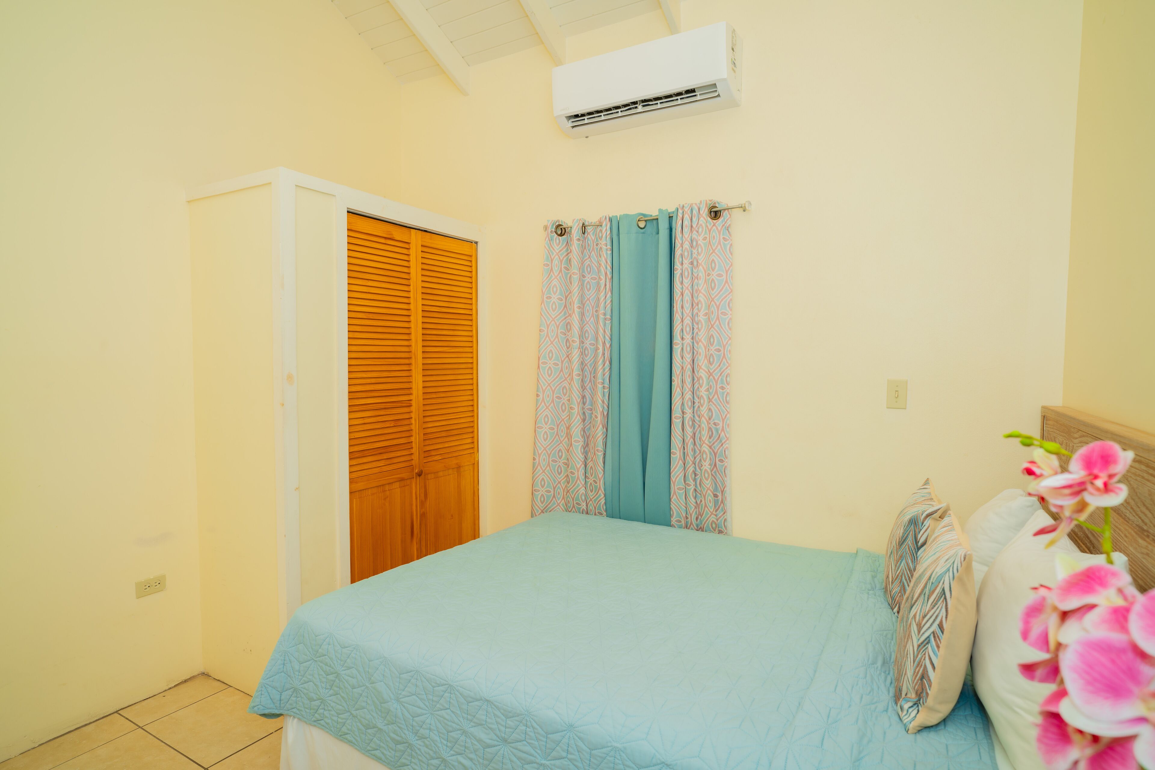 A bedroom with a bed, curtains, a wooden door, and an air conditioning unit.