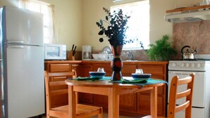 A kitchen with wooden cabinets, a white refrigerator, a stove, and a dining table with chairs. - Connie's Comfort Suites (St. John's)