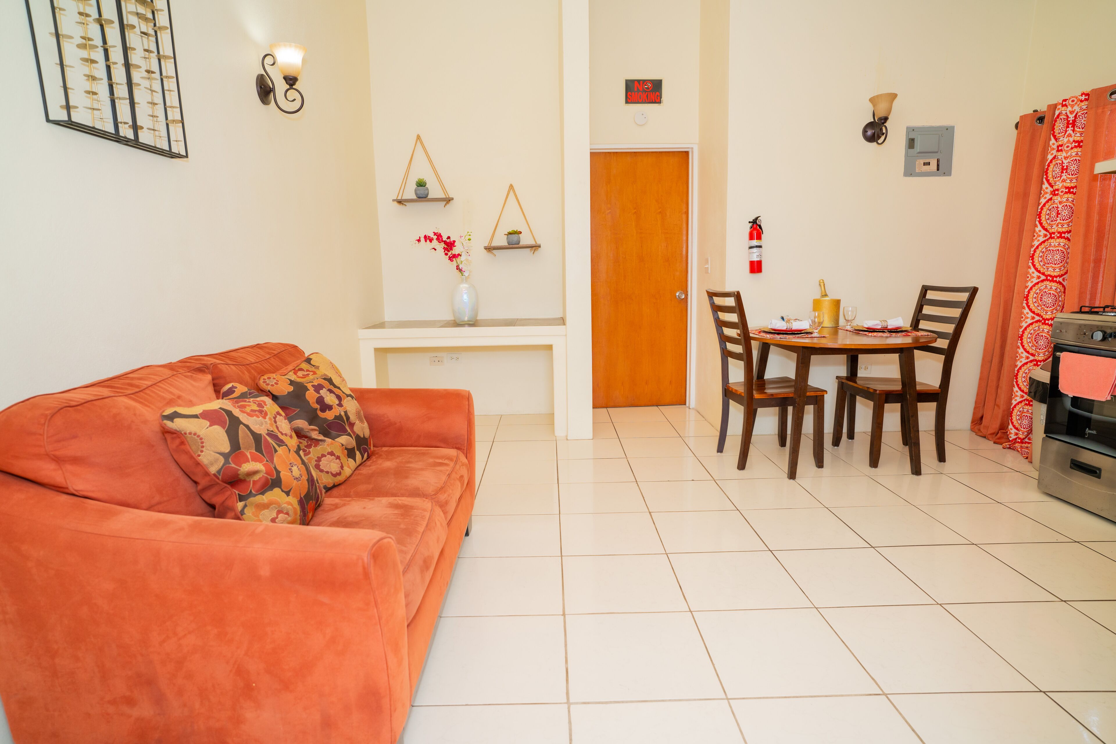 A living room with a sofa, a dining table with chairs, a kitchen area, and a door.