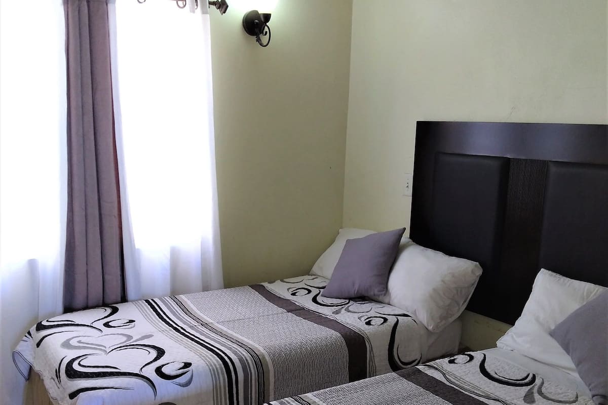 A hotel room with two beds, each with patterned bedding, a headboard, and a wall-mounted light fixture.
