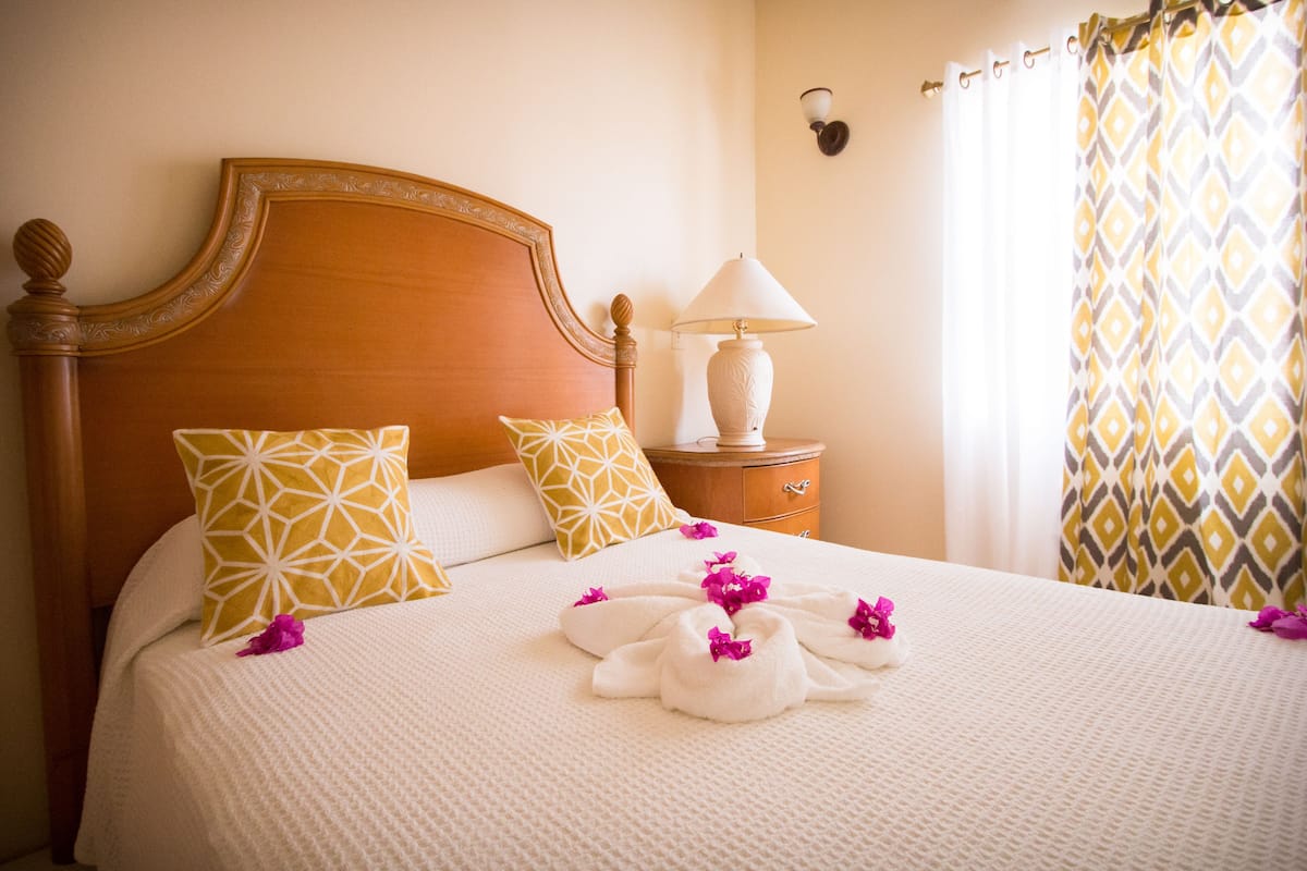 A neatly made bed with patterned pillows, a bedside lamp, and a decorative wall light.