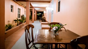 A corridor with a wooden table and chairs, a vase with flowers, and potted plants along the walls. - Connie's Comfort Suites (St. John's)