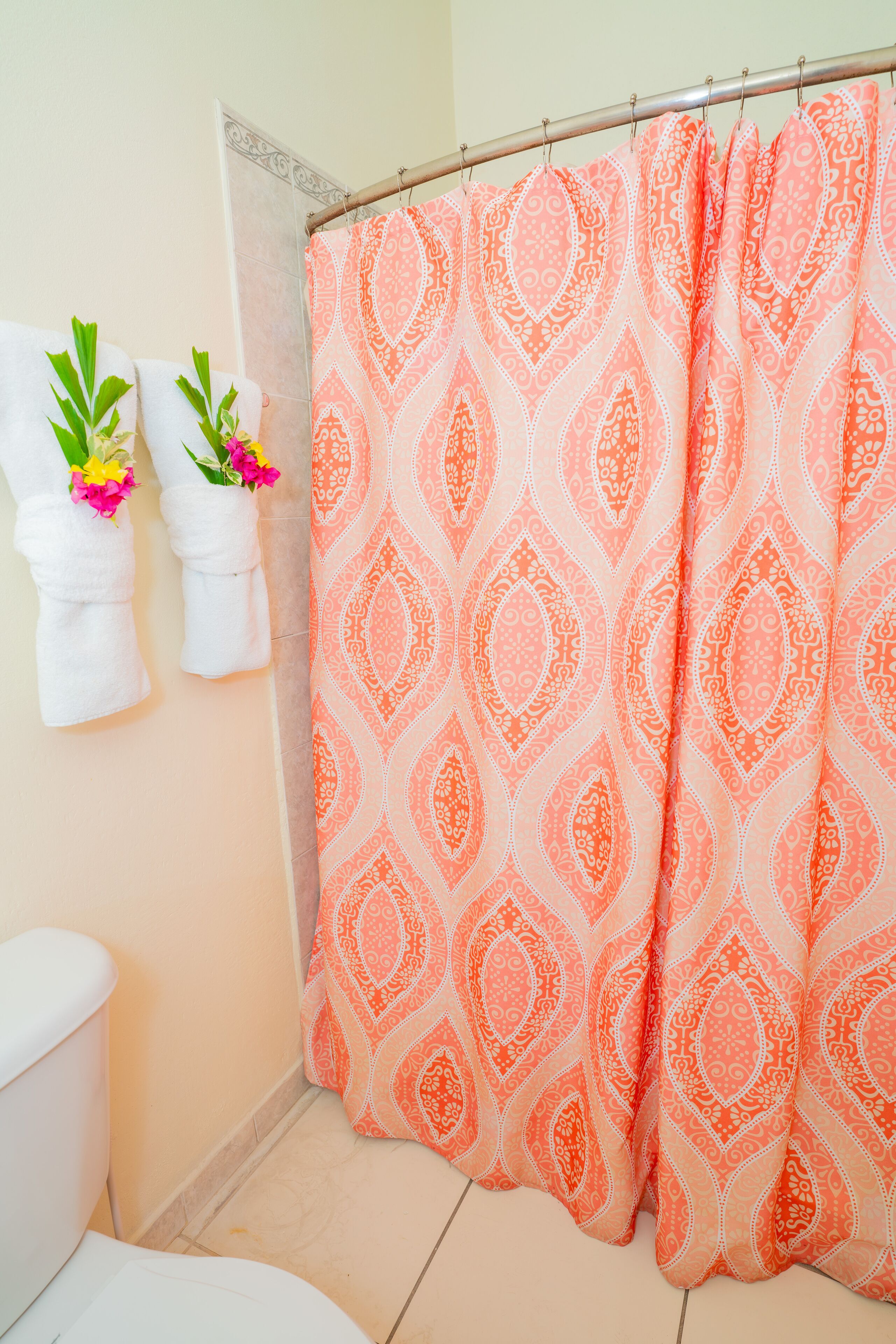 A bathroom with a shower curtain, two towels with flowers, and a toilet.