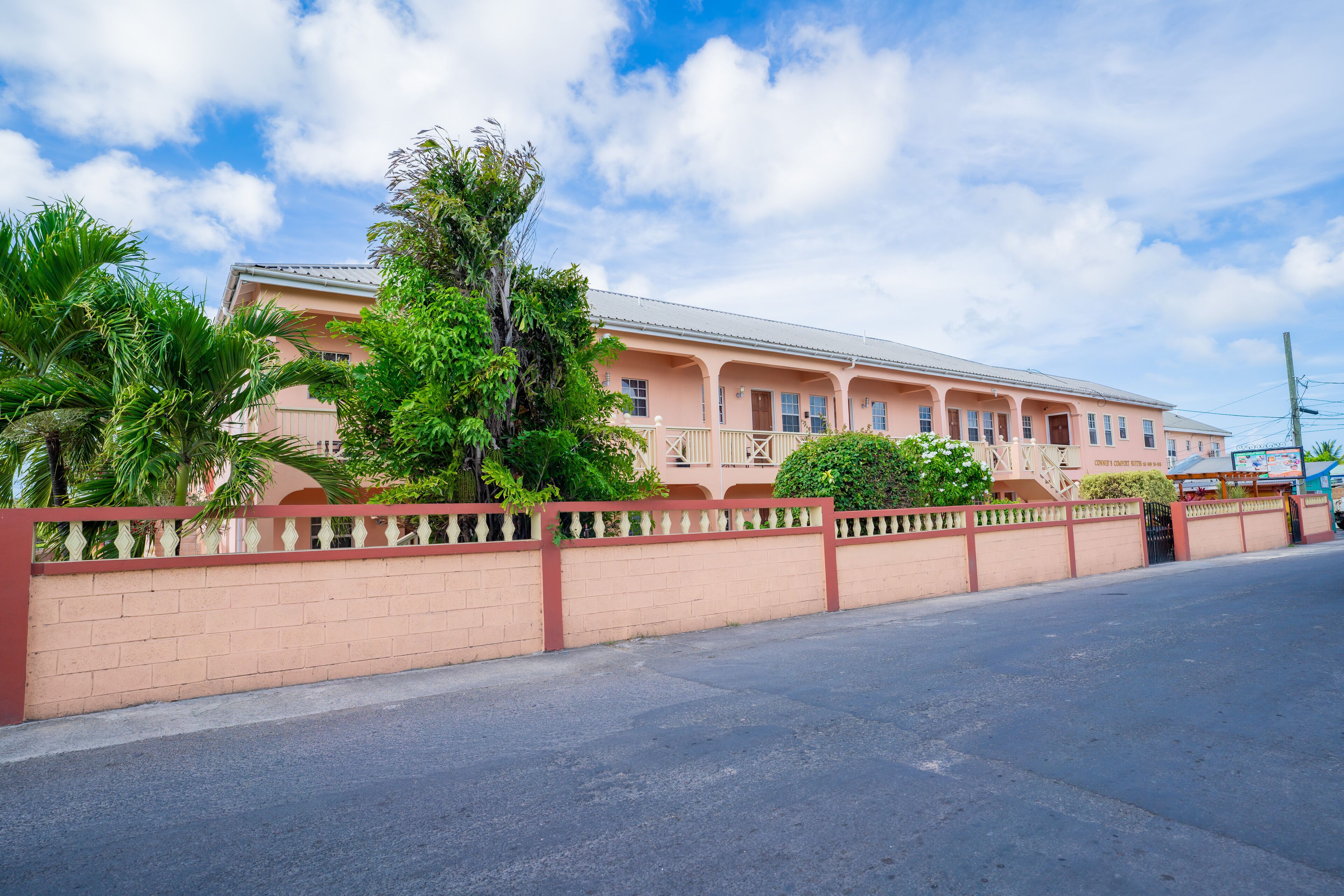 A pink building with a balcony, surrounded by a red fence and greenery.