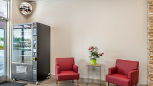 A room with a vending machine, two red chairs, a small table with a potted plant, and a mirror on the wall. - Red Roof Inn Richmond, VA (Richmond)