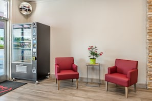 A room with a vending machine, two red chairs, a small table with a potted plant, and a mirror on the wall. - Red Roof Inn Richmond, VA (Richmond)