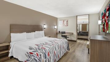 A hotel room with a bed, a desk, a chair, a small table, and a mirror.