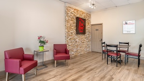 A reception area with a stone wall, a Red Roof Inn sign, a reception desk, and a seating area with chairs and a table. - Red Roof Inn Richmond, VA (Richmond)