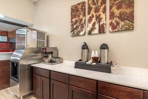 A kitchenette with a stainless steel refrigerator, a coffee machine, and a coffee dispenser. There are wooden cabinets and a countertop. - Red Roof Inn Richmond, VA (Richmond)