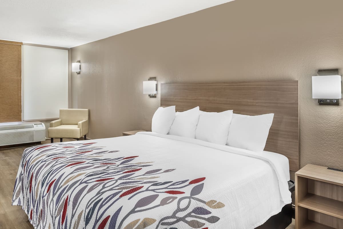 A hotel room with a large bed, a chair, a nightstand, and wall-mounted lights.