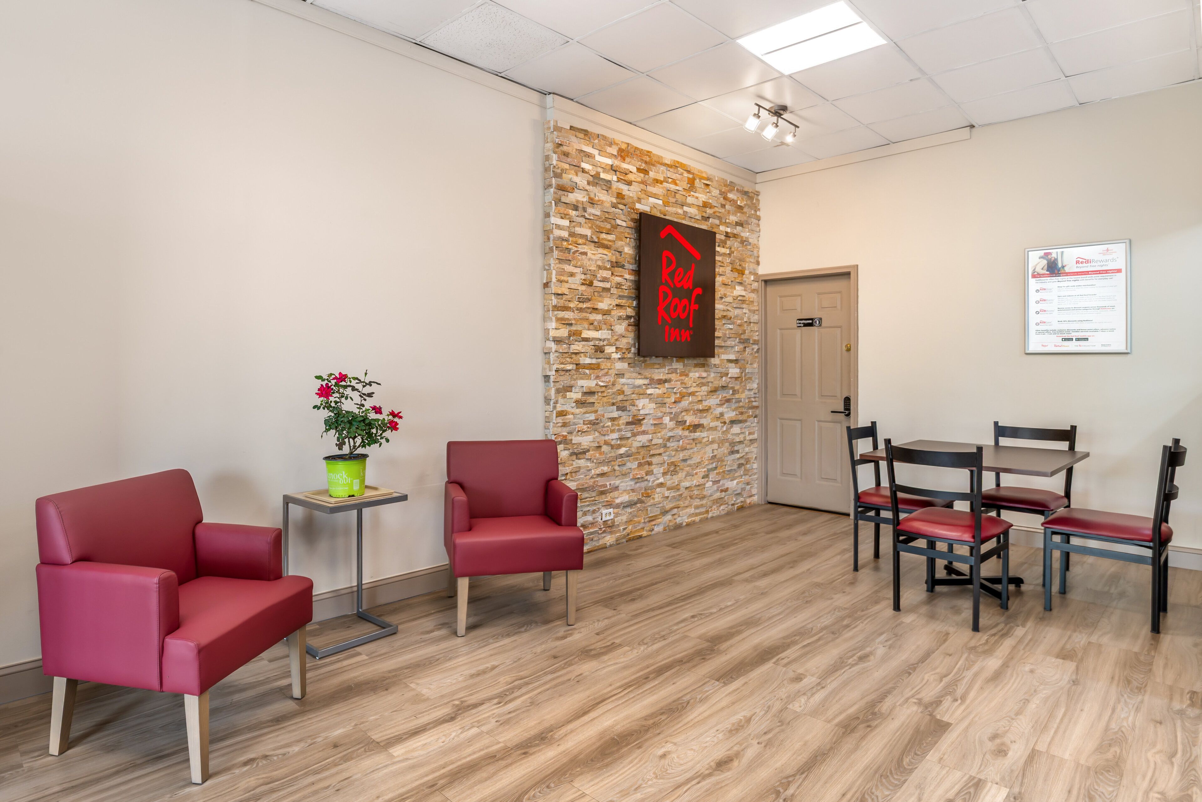 A reception area with a stone wall, a Red Roof Inn sign, a reception desk, and a seating area with chairs and a table.