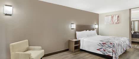 A hotel room with a bed, a chair, a nightstand, and a wall-mounted light fixture.