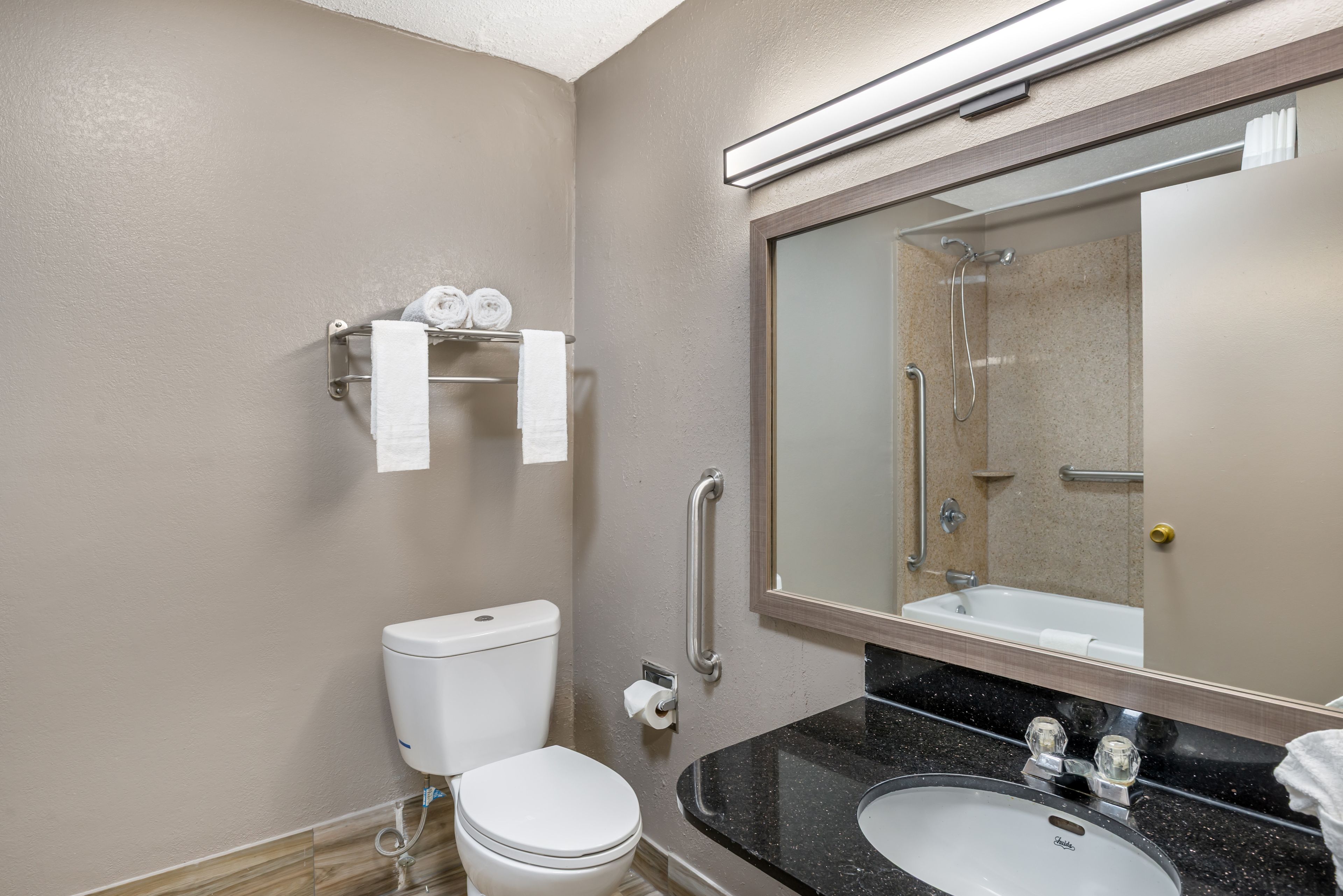 A bathroom with a toilet, sink, mirror, towel rack, and grab bars.